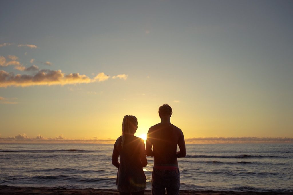 A male and female silhouette in front of the ocean